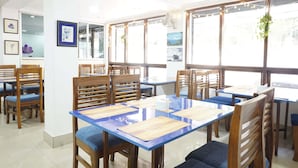 A restaurant with wooden tables and chairs, large windows, and framed artwork on the walls. - Hotel Aster (Gangtok)