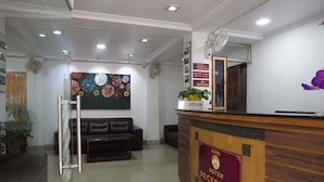 A hotel reception area with a wooden reception desk, a reception sign, a colorful floral mural, a leather sofa, and a potted plant. - Hotel Aster (Gangtok)