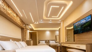 Une chambre d’hôtel moderne avec un grand lit, un canapé, une table en bois sur laquelle sont posés deux verres de jus d’orange, une télévision et un miroir.