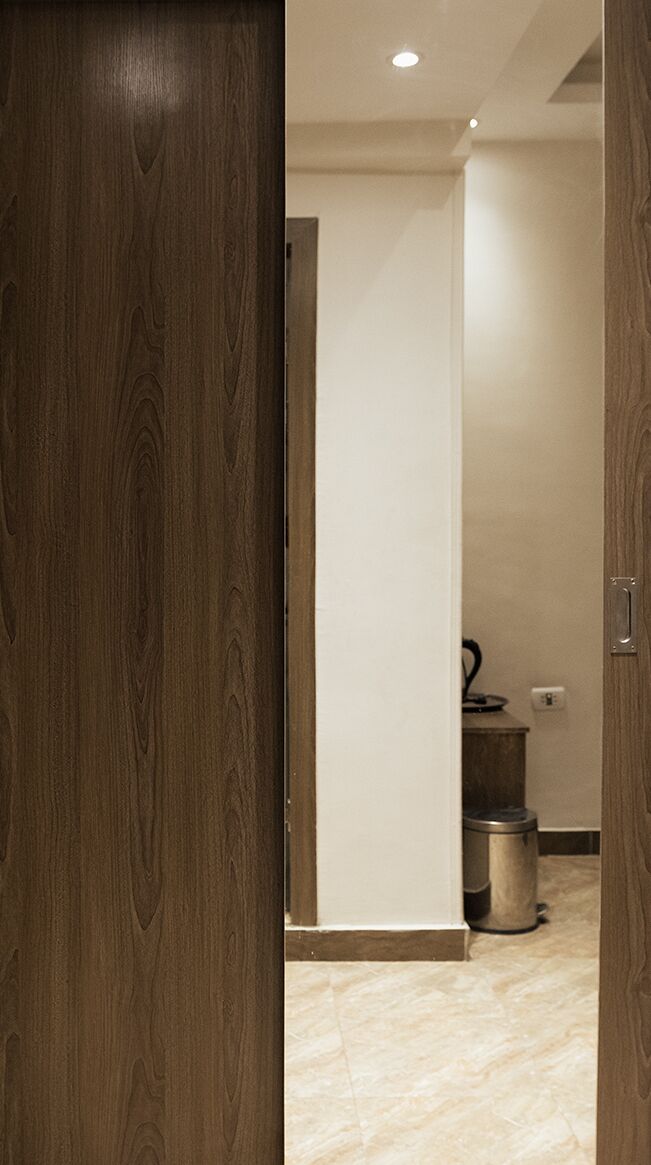 A hallway with a wooden door, a white wall, and a trash bin.