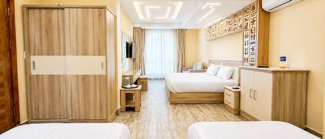 A hotel room with two beds, a desk, a TV, a minibar, and a wall with hieroglyphs.