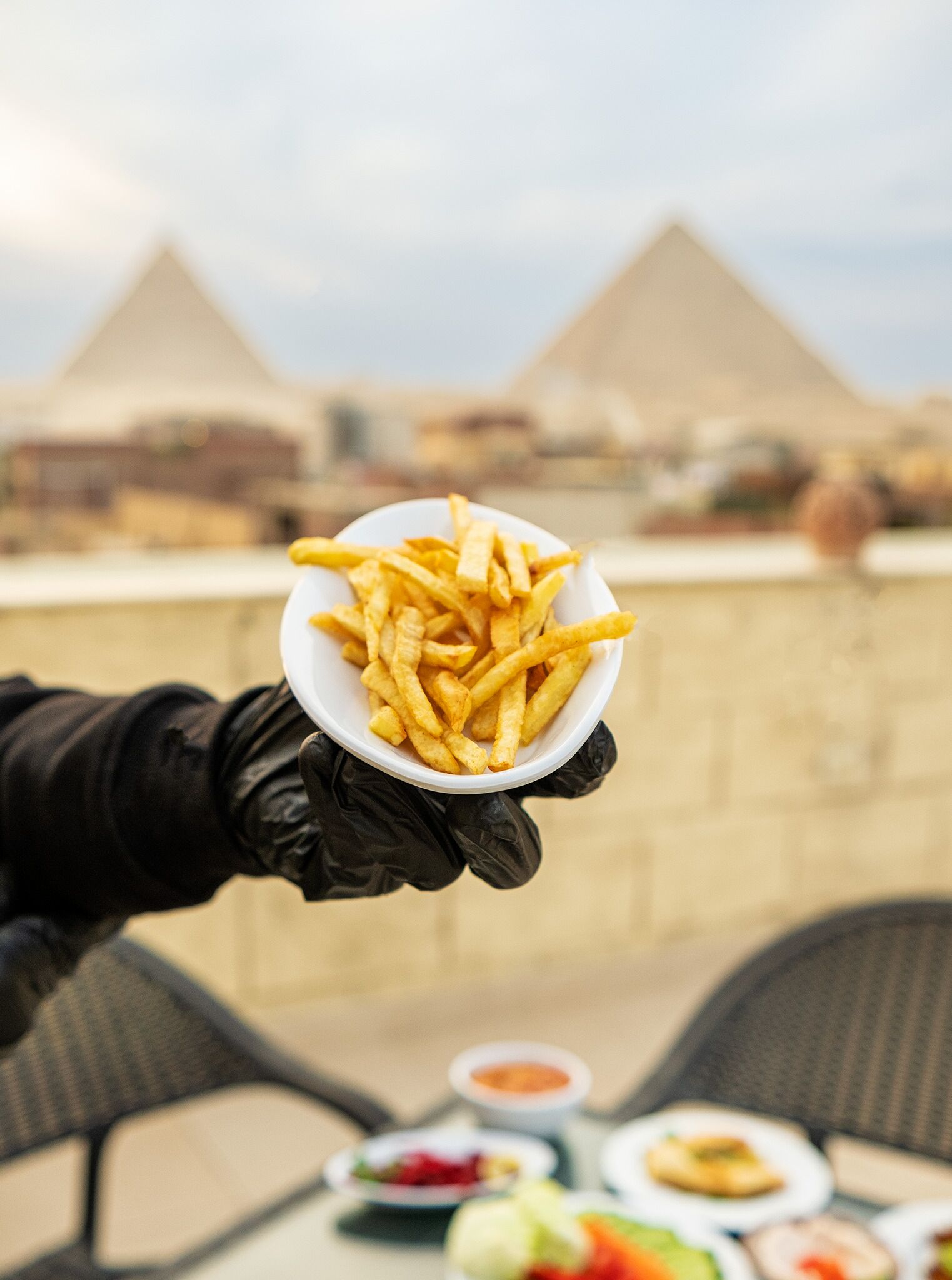 A person holding a bowl of fries with a view of pyramids in the background.