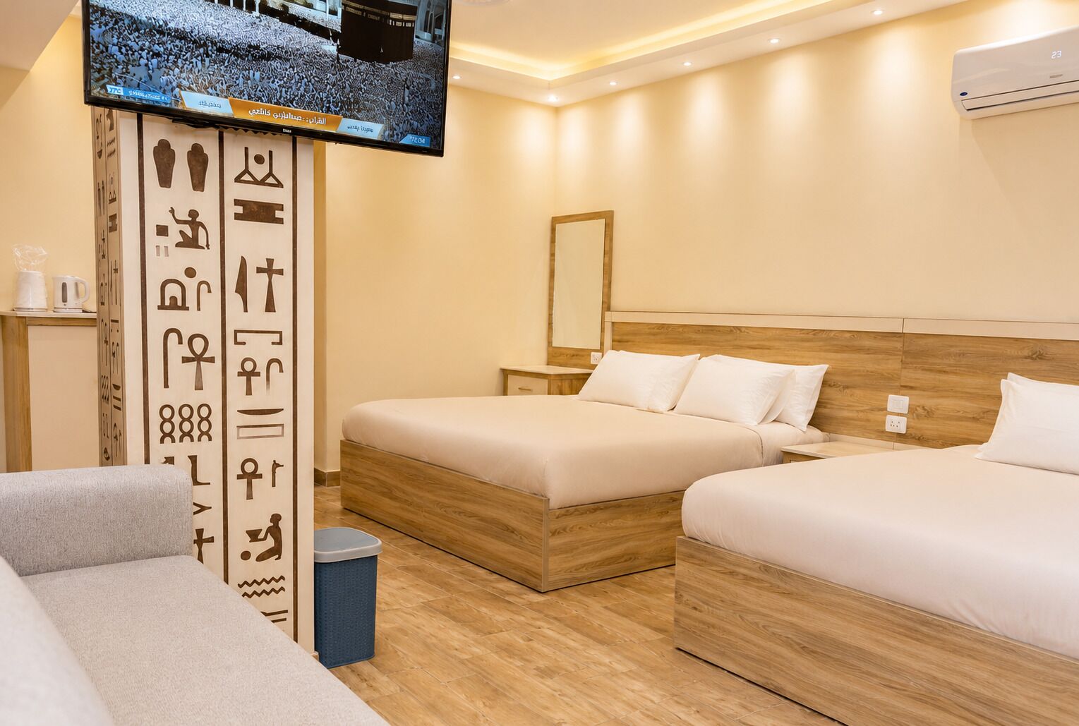 Een hotelkamer met twee bedden, een televisie, een muur met hiërogliefen en een prullenbak.