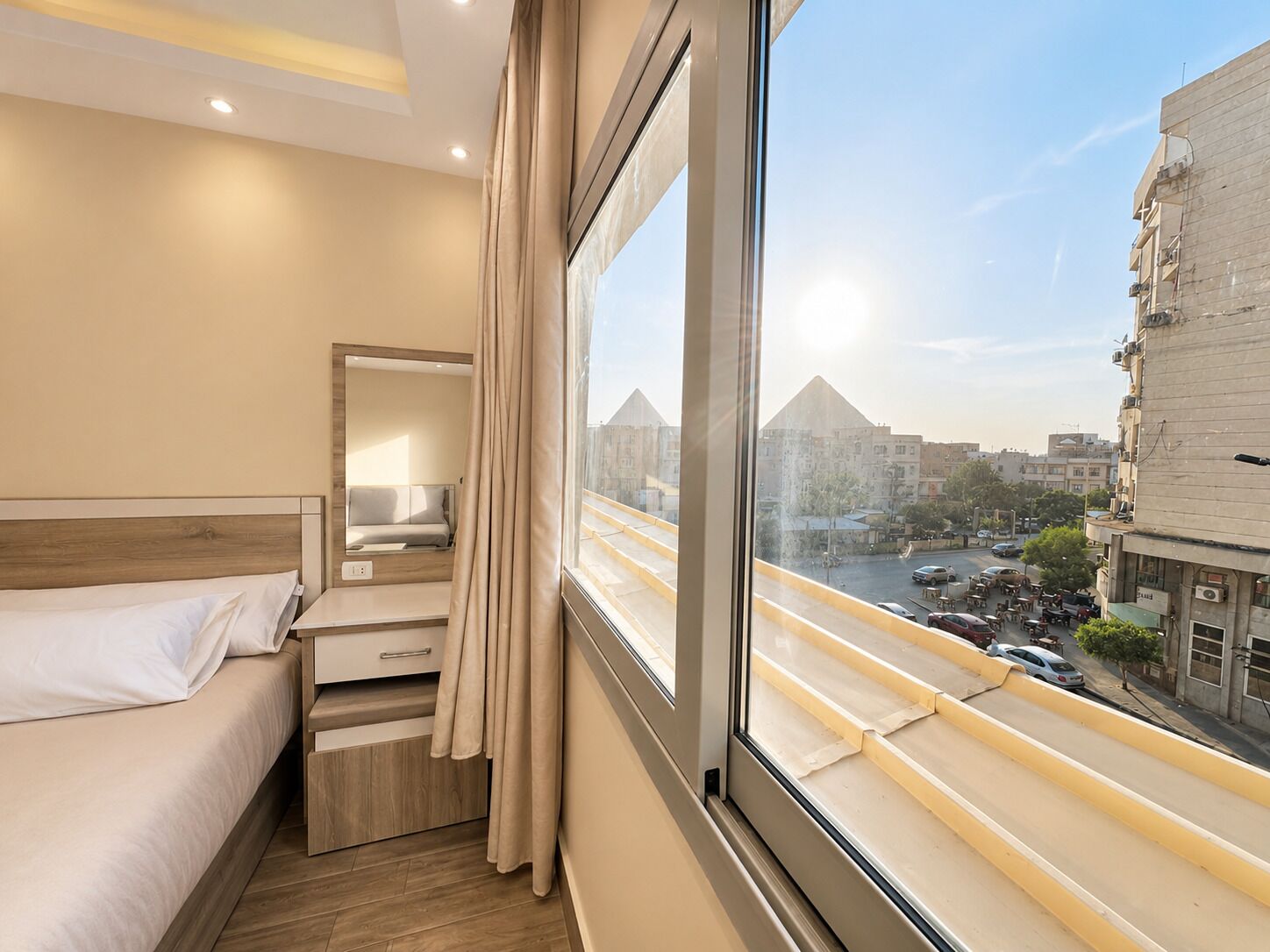 A hotel room with a bed, a desk, a mirror, and a large window offering a city view.