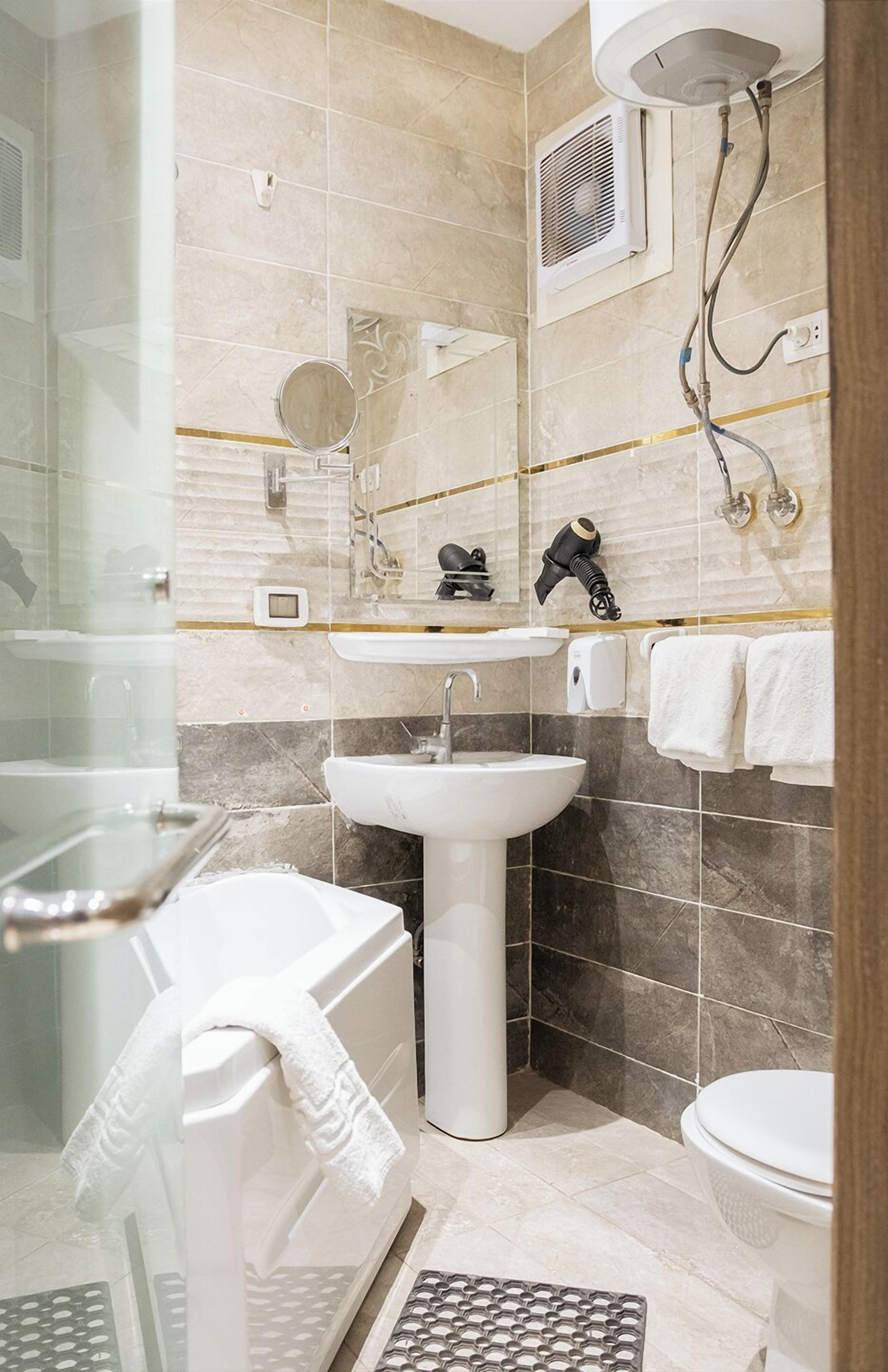 A modern bathroom with a glass shower enclosure, a pedestal sink, a handheld hairdryer, and a toilet.