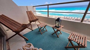 A balcony with wooden lounge chairs, a small table with a lantern, and a view of the beach. - Perfect vacation getaway Ocean ViewnWifi (Cancun)