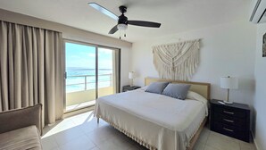 A hotel room with a bed, a ceiling fan, a nightstand with a lamp, a macrame wall hanging, and a view of the ocean through a sliding door. - Perfect vacation getaway Ocean ViewnWifi (Cancun)