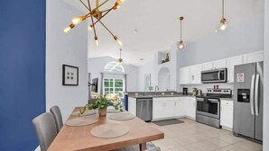 A modern kitchen with white cabinets, stainless steel appliances, and a dining area with a wooden table and chairs. - NEW*4 Bdrm, 3 Bath* Updated Detached Pool Home, 10 Minutes to Disney (Kissimmee)