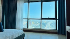 A bedroom with a large window, a bed, and a view of a cityscape. - Fairview Luxury Apartments (Dar es Salaam)