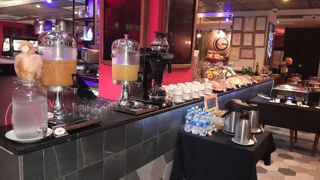 Montaje tipo bufé con varios dispensadores de comida y bebida, incluyendo una máquina de café y un dispensador de líquidos.