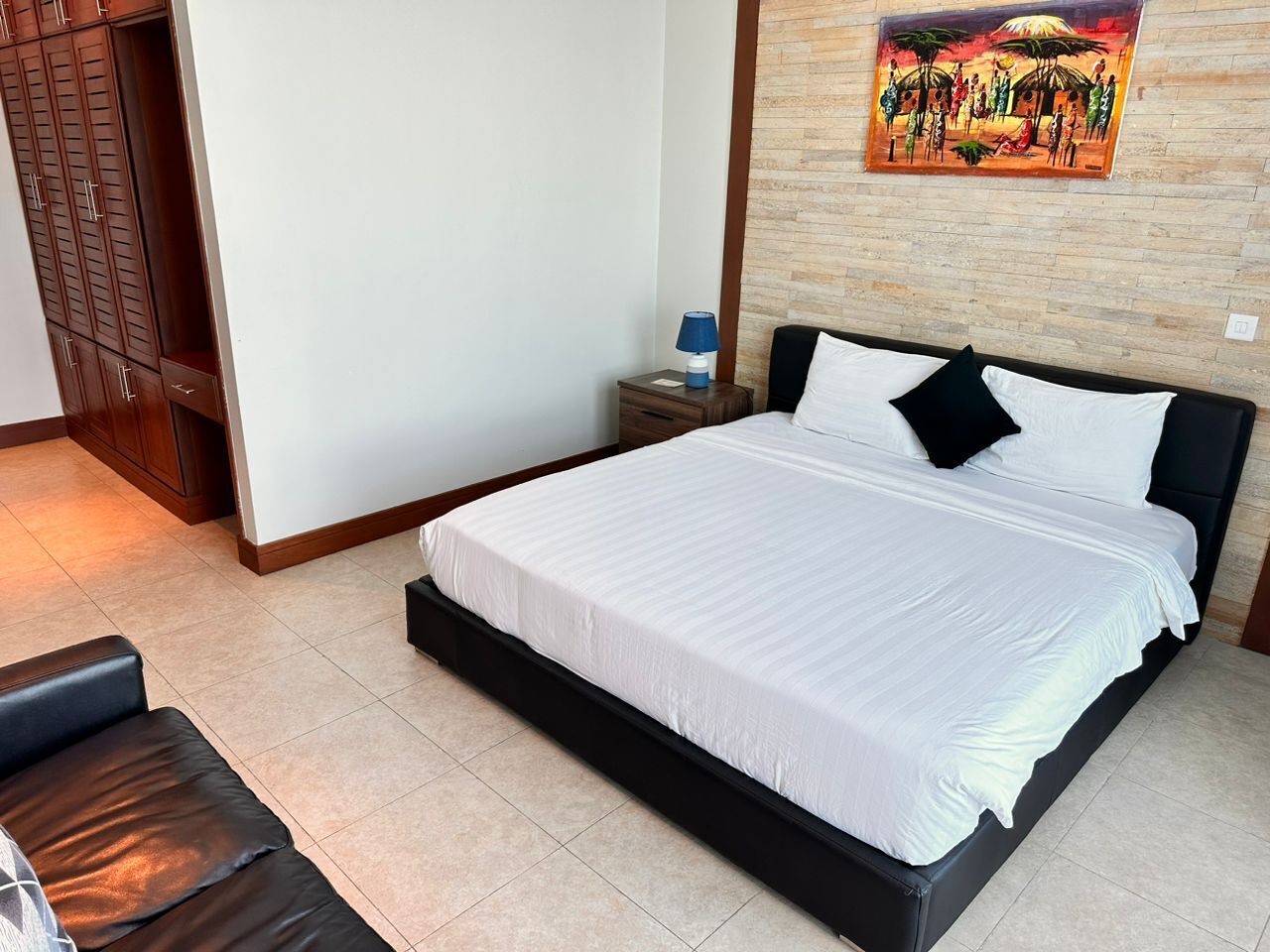 A neatly made bed with white linens, a black headboard, and a nightstand with a blue lamp.