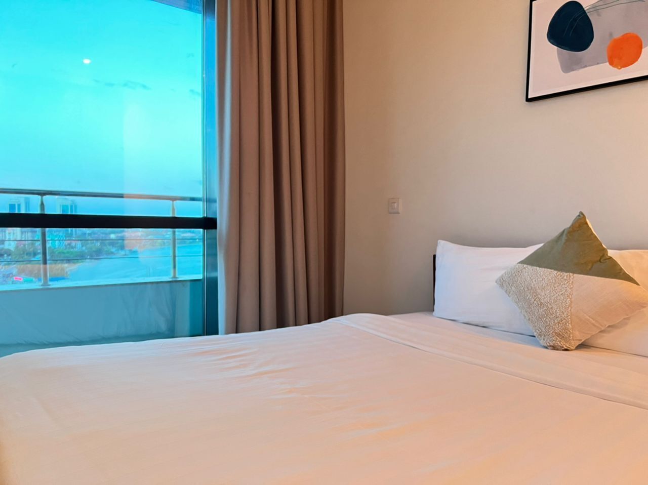 Une chambre d’hôtel avec un grand lit, une fenêtre avec des rideaux et une œuvre d’art abstraite encadrée accrochée au mur.
