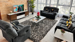 A modern living room with a large window, a black sofa, a grey armchair, and a coffee table with a plant. - Fairview Luxury Apartments (Dar es Salaam)