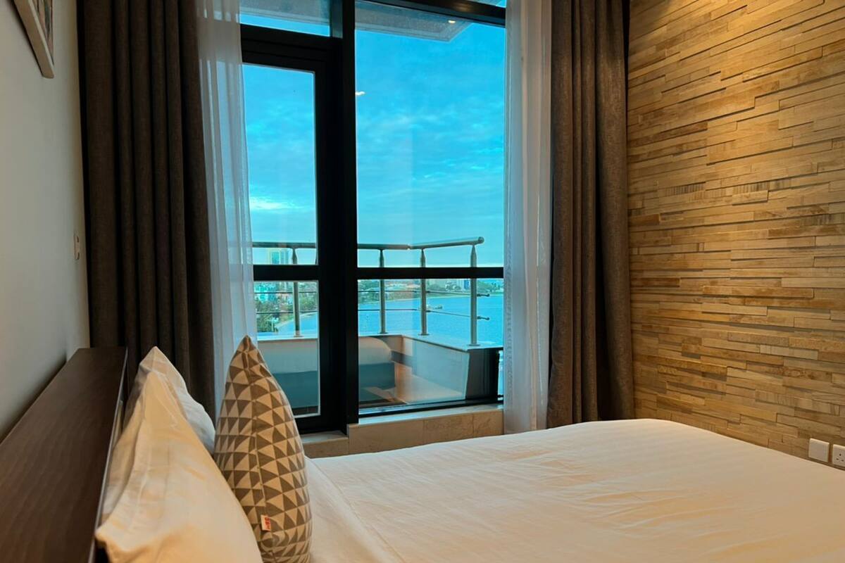 Een hotelkamer met een bed, uitzicht op de zee via een balkon, en een houten wand.