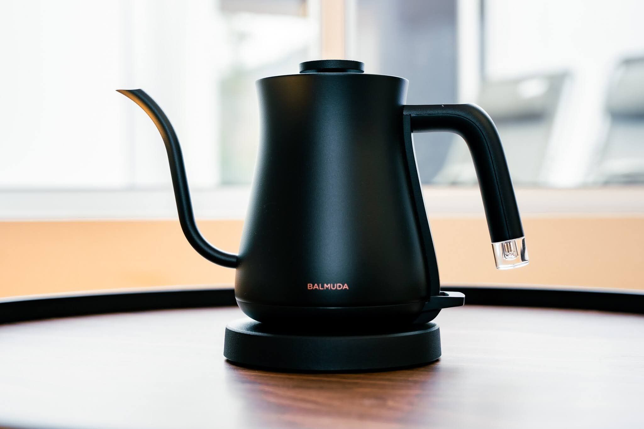 A black electric kettle on a table with a window in the background.