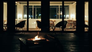 A fire feature in a dimly lit room with large windows, wooden flooring, and modern furniture. - BLANC FUJI (Fujiyoshida)