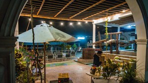An outdoor patio area with tables and chairs, surrounded by potted plants and a large umbrella. - Glamping Toneles y Viñedos (San Juan Bautista)