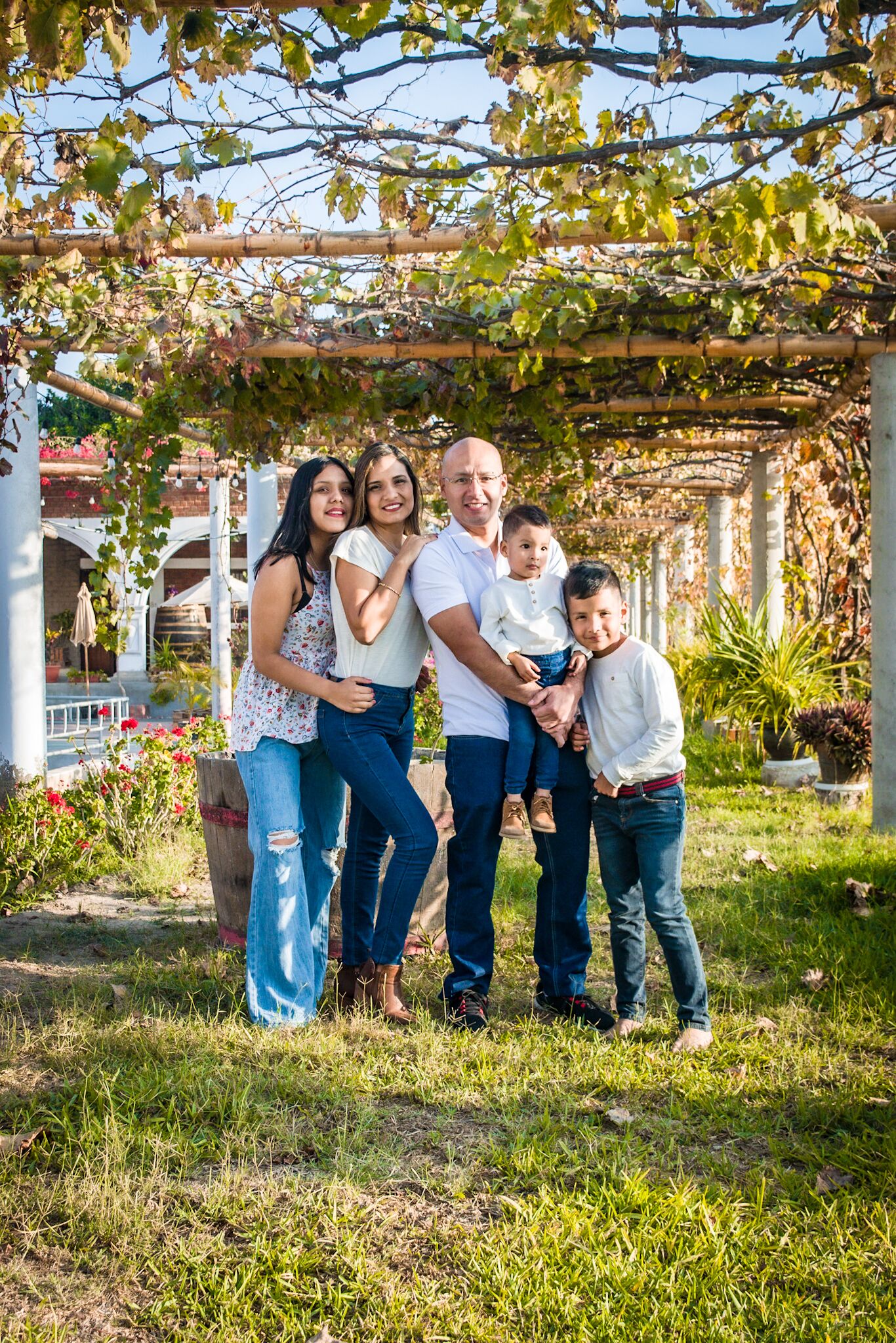 A family of four standing under a pergola with a garden in the background.