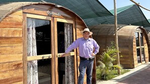 A wooden structure with a sign reading "Quebranta" and a person standing at the entrance. - Glamping Toneles y Viñedos (San Juan Bautista)