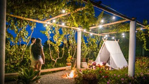 Un jardín con un pozo de fuego, una carpa blanca y luces colgantes.