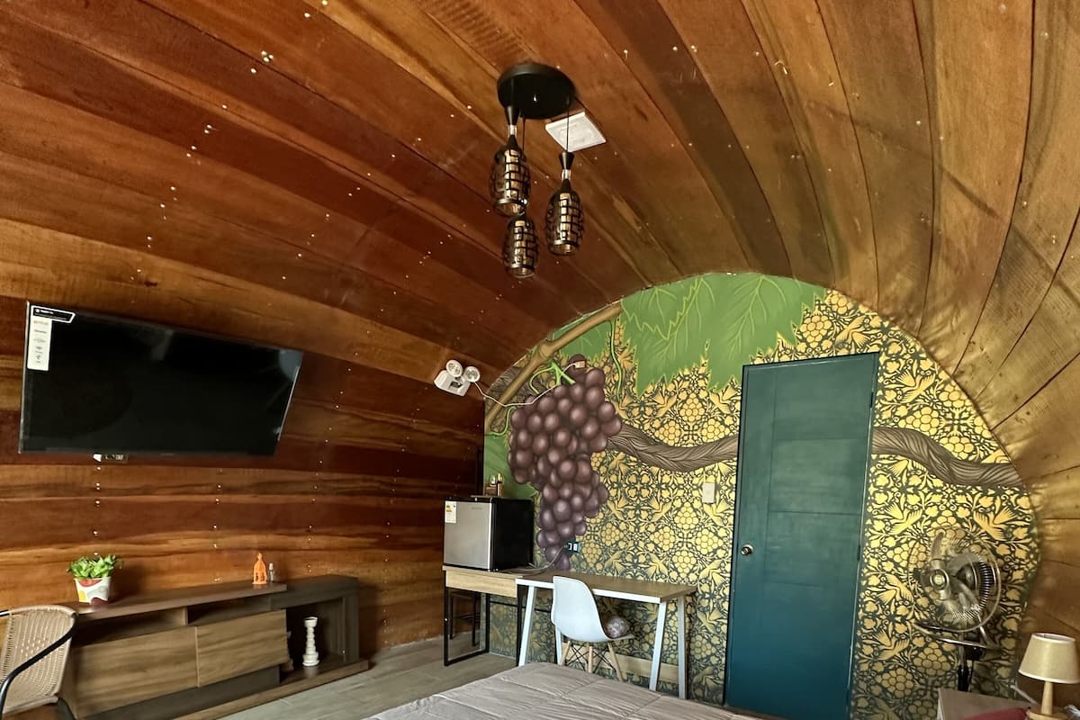 A bedroom with a large bed, wooden ceiling, a desk, and a TV.