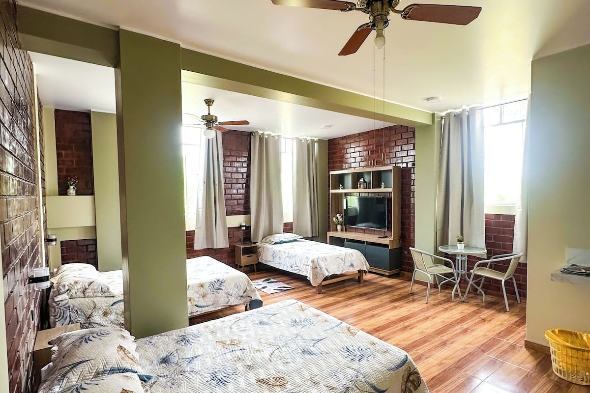 A hotel room with two beds, a TV, a small table with chairs, and a ceiling fan.