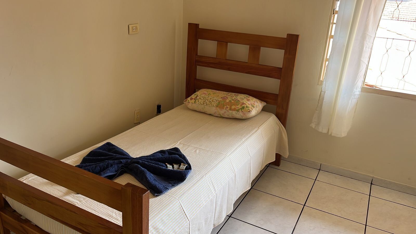A small, single-bed room with a wooden headboard, a floral pillow, and a blue blanket on the bed.