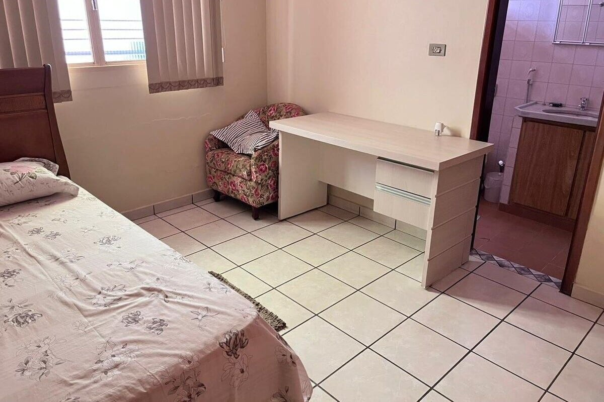 A bedroom with a bed, a desk, a chair, and a small bathroom.