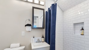A bathroom with a toilet, sink, mirror, and shower curtain. - The Nightingale Nest (Stanwood)