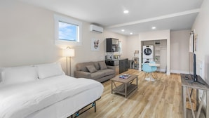 A modern, well-lit room with a bed, a sofa, a coffee table, and a TV. - The Nightingale Nest (Stanwood)