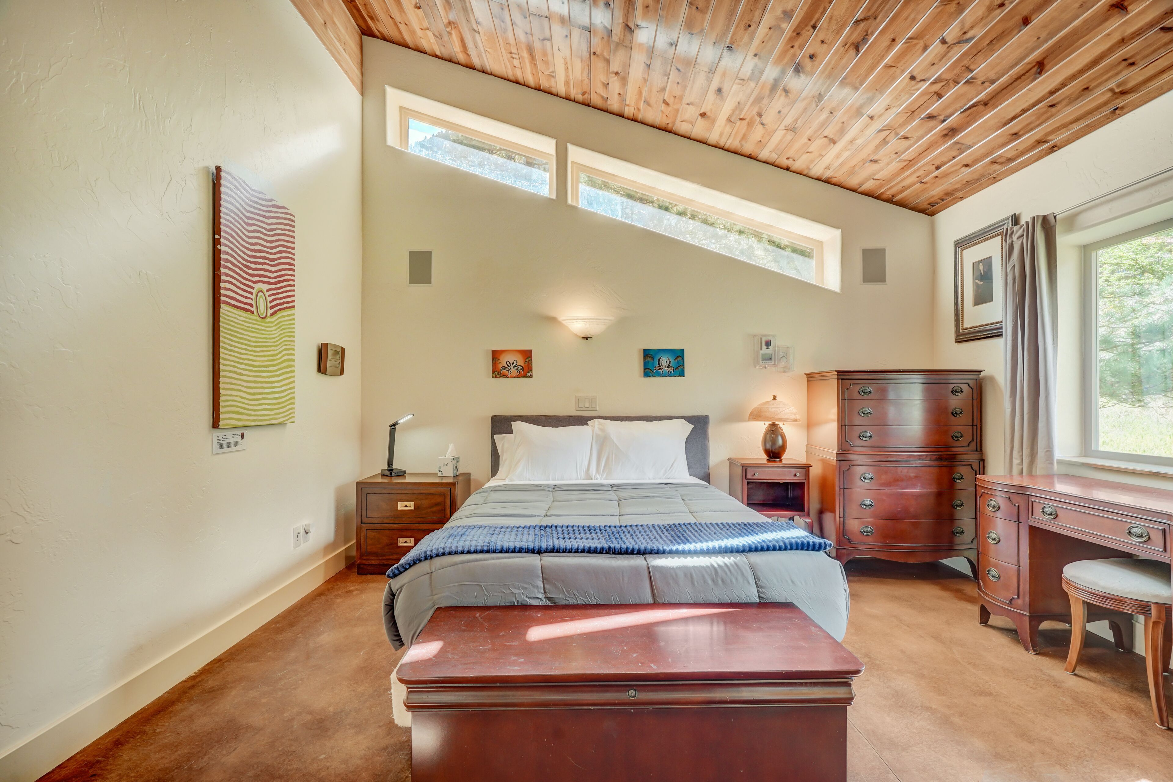 A bedroom with a bed, wooden dresser, desk, and artwork on the walls.