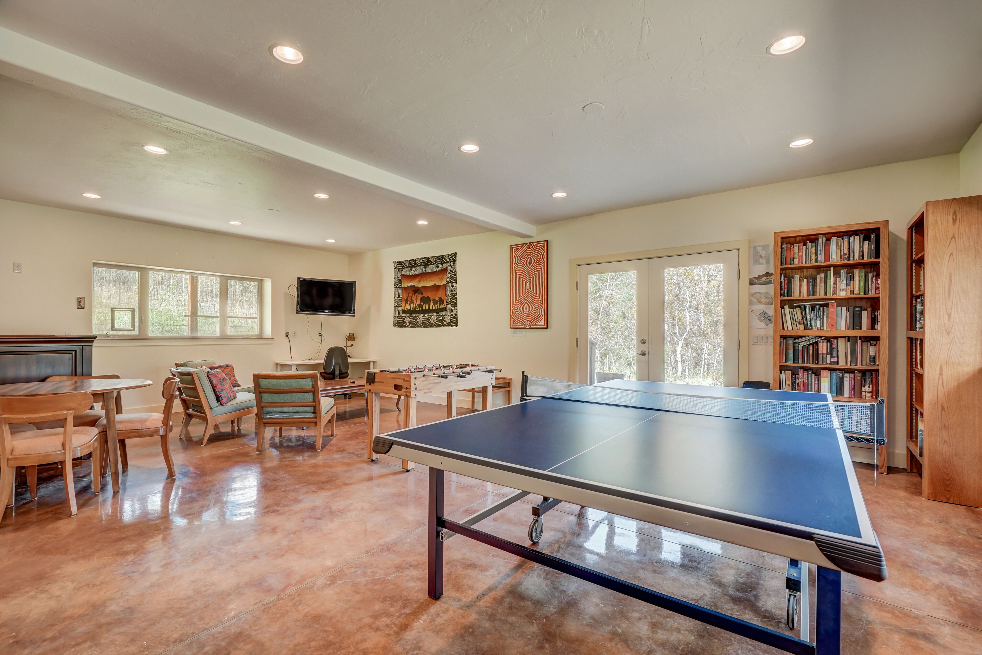 Une pièce spacieuse équipée d’une table de ping-pong, de meubles en bois, d’une bibliothèque et d’un téléviseur.