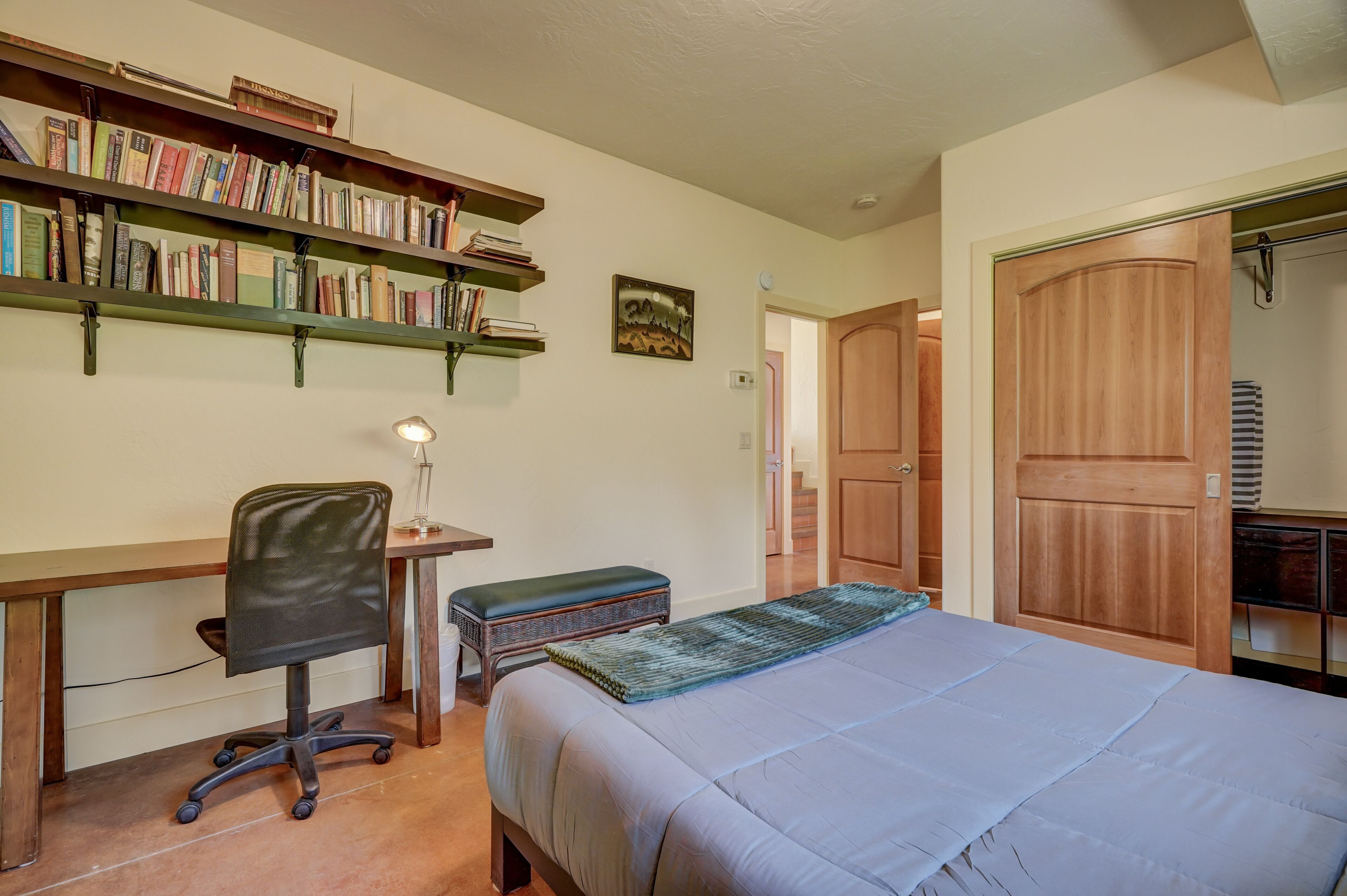 Une chambre à coucher avec un lit, un bureau, une chaise, une bibliothèque et une porte.