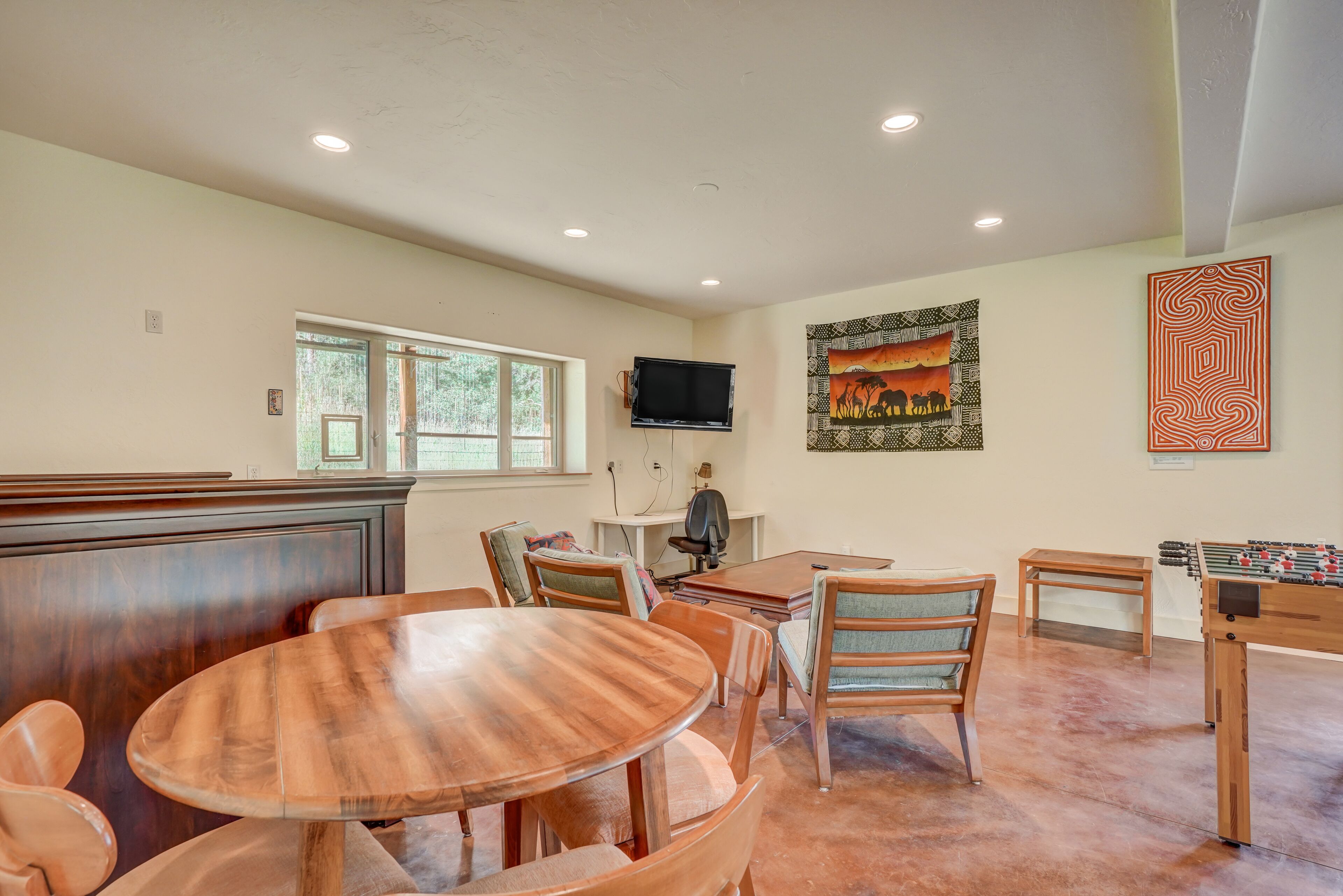 A dining area with a round wooden table and chairs, a television mounted on the wall, and a foosball table.