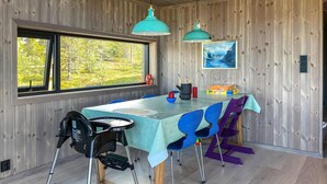 Comedor con mesa preparada para cuatro, paredes de madera, ventana con vista a la vegetación y lámparas colgantes color turquesa.