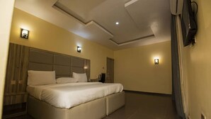 A spacious hotel room with a large bed, a flat-screen TV mounted on the wall, and two wall-mounted light fixtures. - Imperial Boni Hotels and Resorts (Akure)