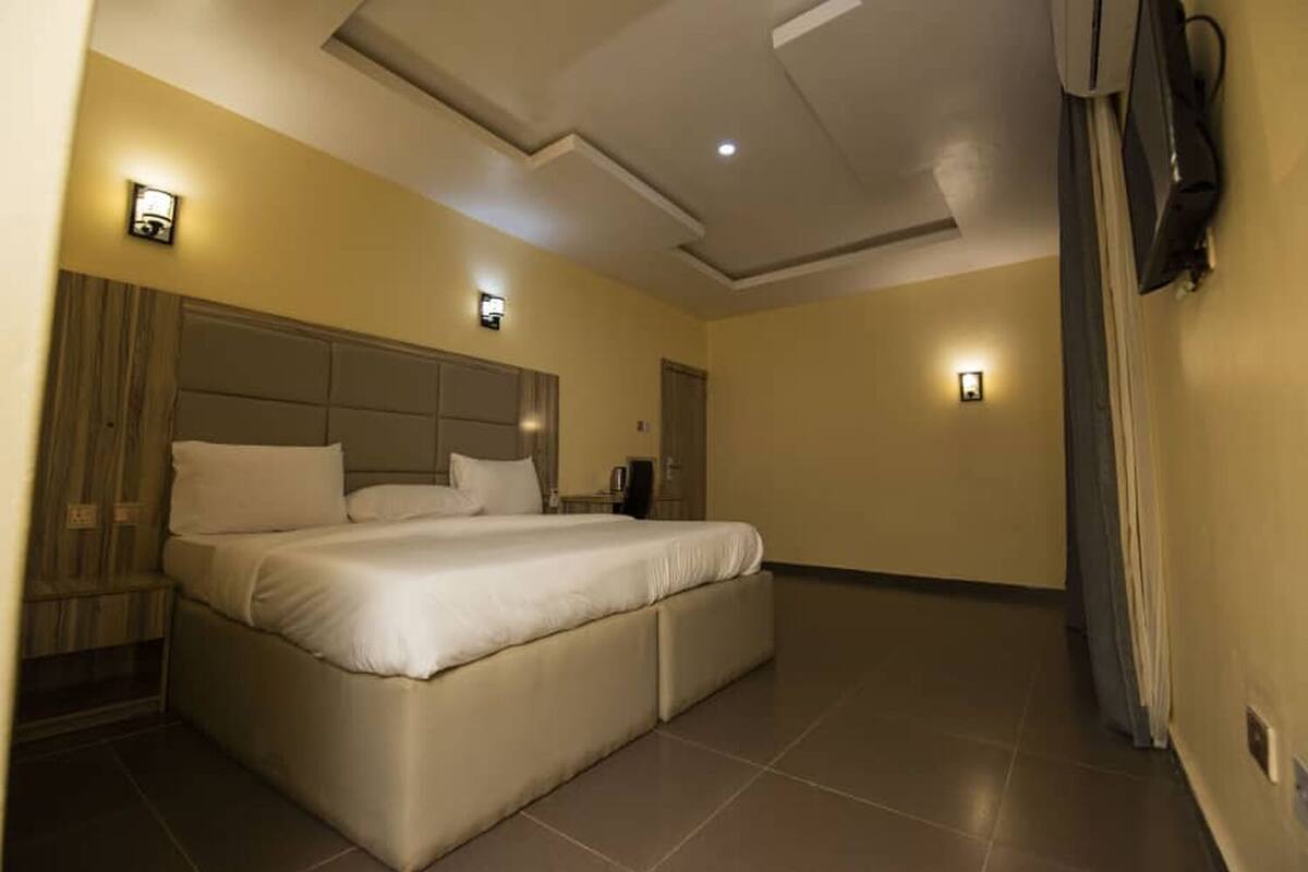 A spacious hotel room with a large bed, a flat-screen TV mounted on the wall, and two wall-mounted light fixtures.
