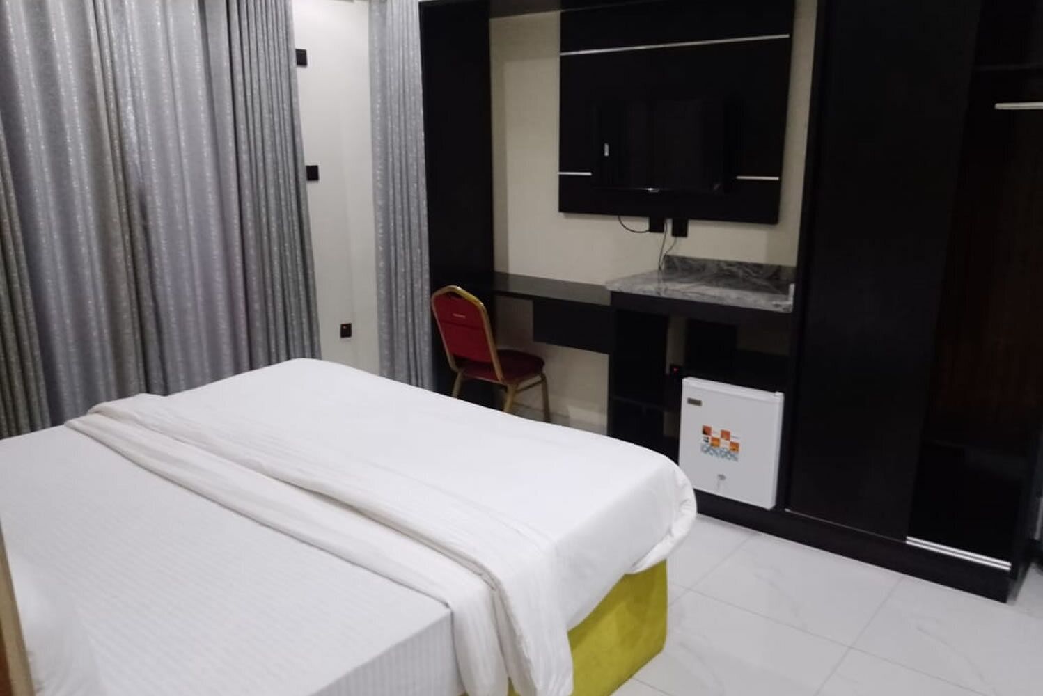 Una habitació d'hotel amb un llit, un escriptori, una cadira i un televisor fixat a la paret.