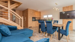 Een moderne keuken met houten kastjes, een eethoek met blauwe bekleden stoelen, en een trap.