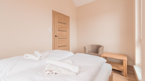 A bedroom with two beds, a wooden door, a chair, and a small wooden table. - Apartamenty Sun & Snow Baltic Garden (Sztutowo)