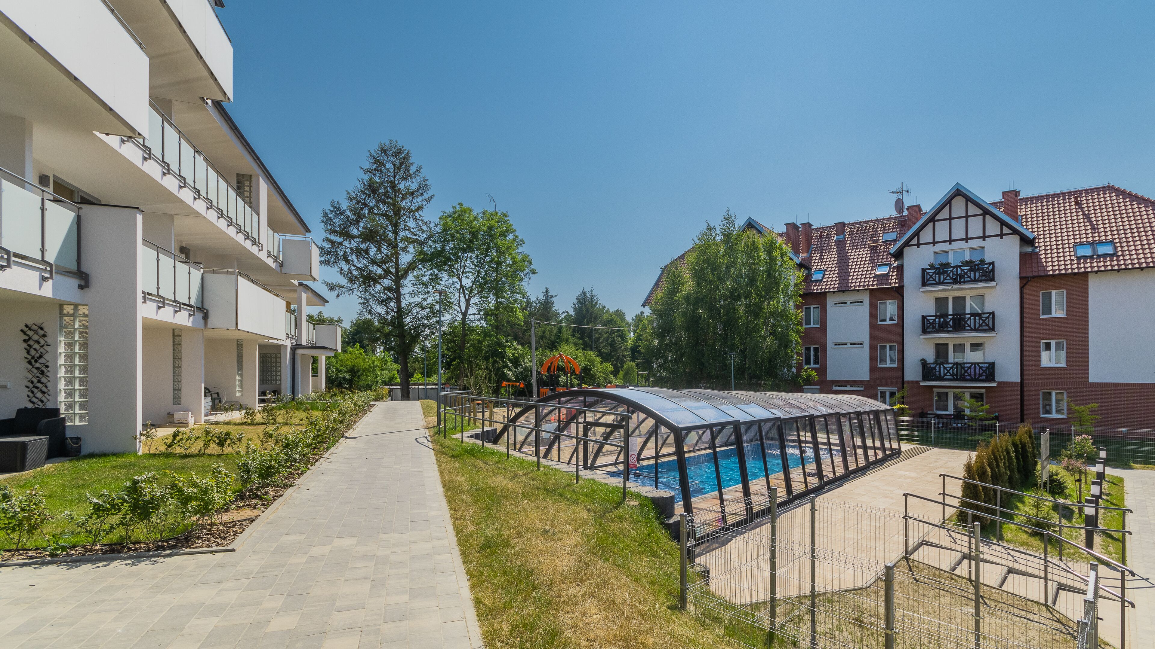 A modern apartment complex with a swimming pool, covered outdoor seating, and a well-maintained garden.