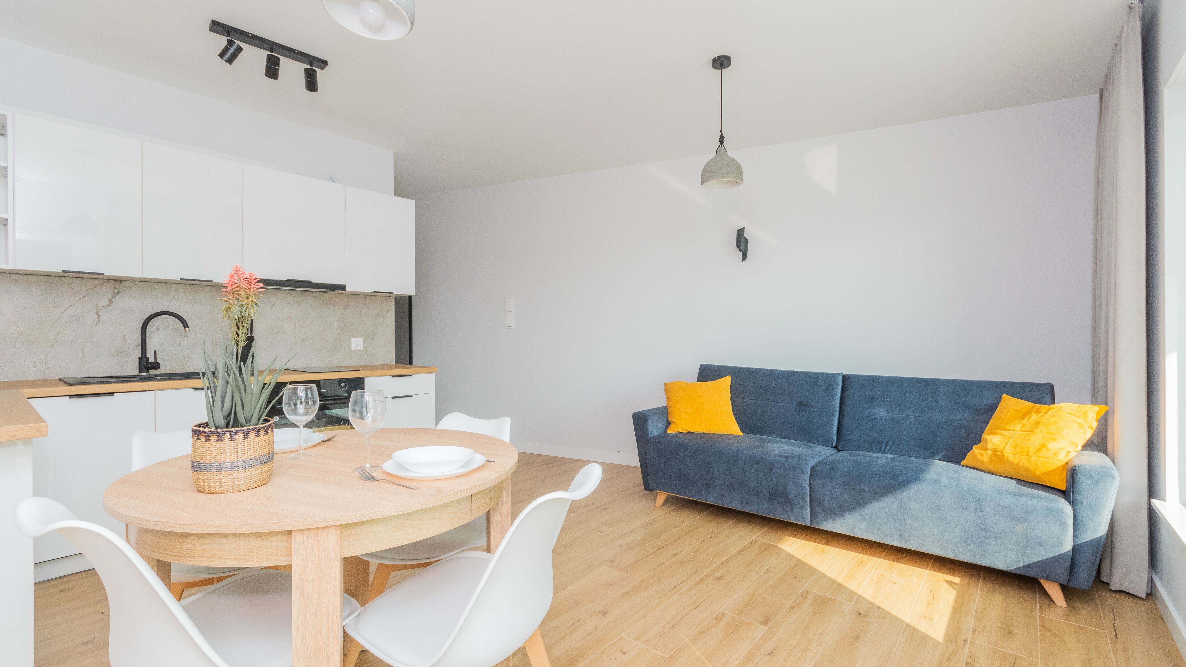 A modern living space with a kitchen, dining area, and a blue sofa with yellow cushions.