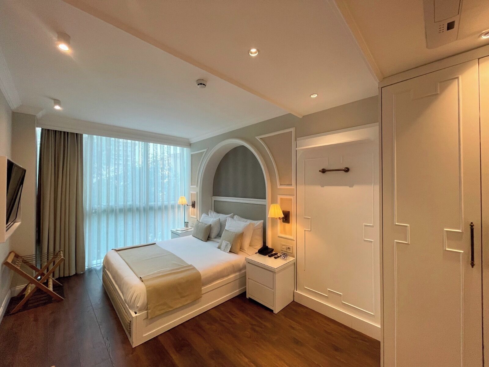 Una habitación de hotel con una cama grande, mesitas de noche, un televisor y un armario.