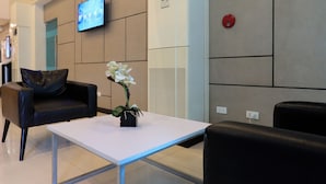 A modern waiting area with a flat-screen TV, a white table, and black leather chairs. - Hotel Sogo Fairview  (Quezon City)