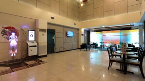 A spacious lobby with a digital kiosk, a flat-screen TV, and a seating area with tables and chairs. - Hotel Sogo Fairview  (Quezon City)
