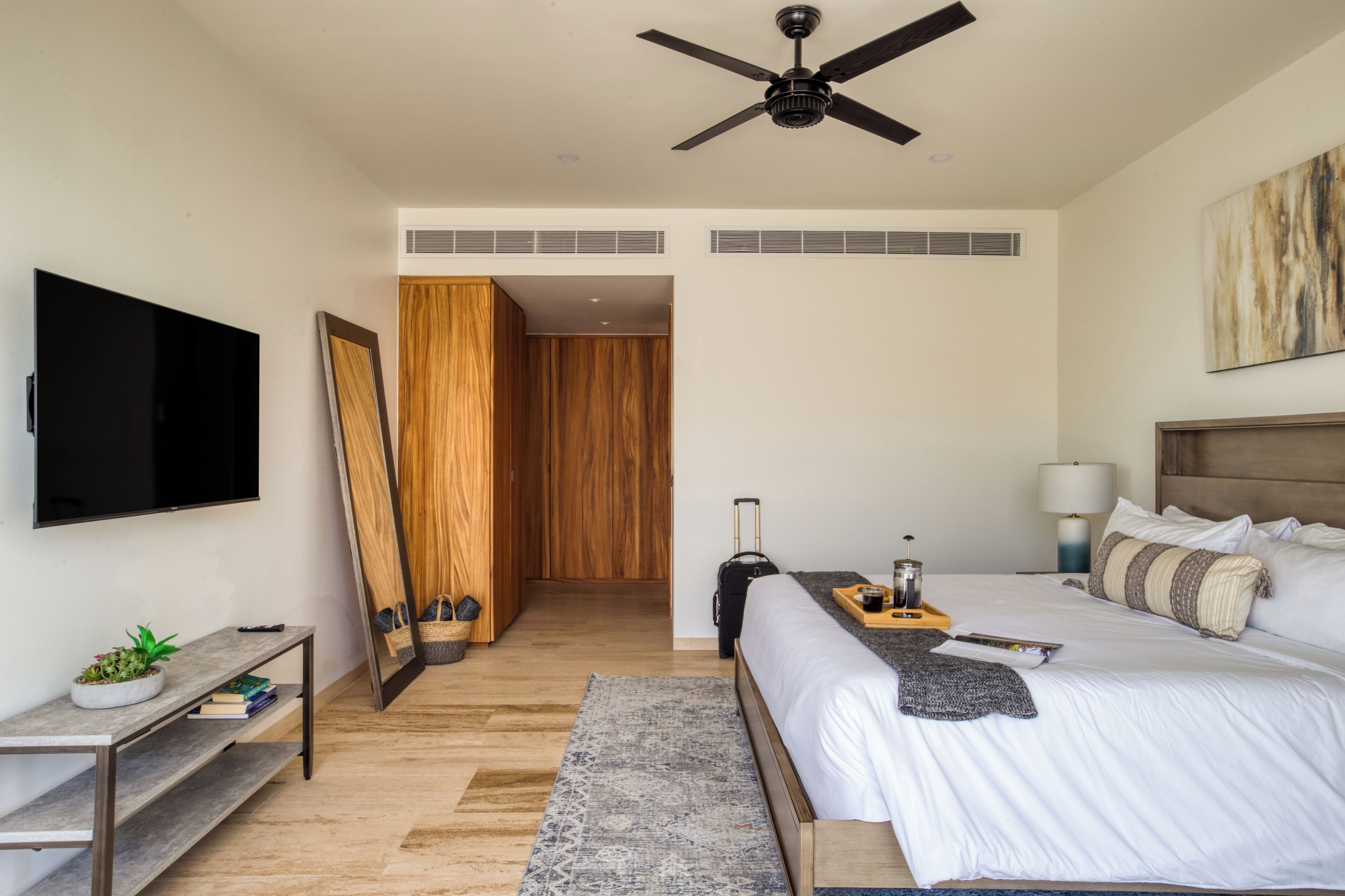 A modern hotel room with a bed, bedside table, TV, and a ceiling fan.