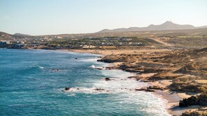 A coastal town with a beach, rocky shoreline, and distant mountains. - Marella Cabo (Cabo San Lucas)