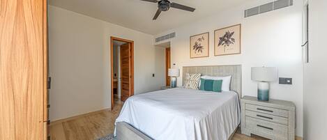 A bedroom with a bed, bedside tables, a ceiling fan, and framed artwork on the wall.