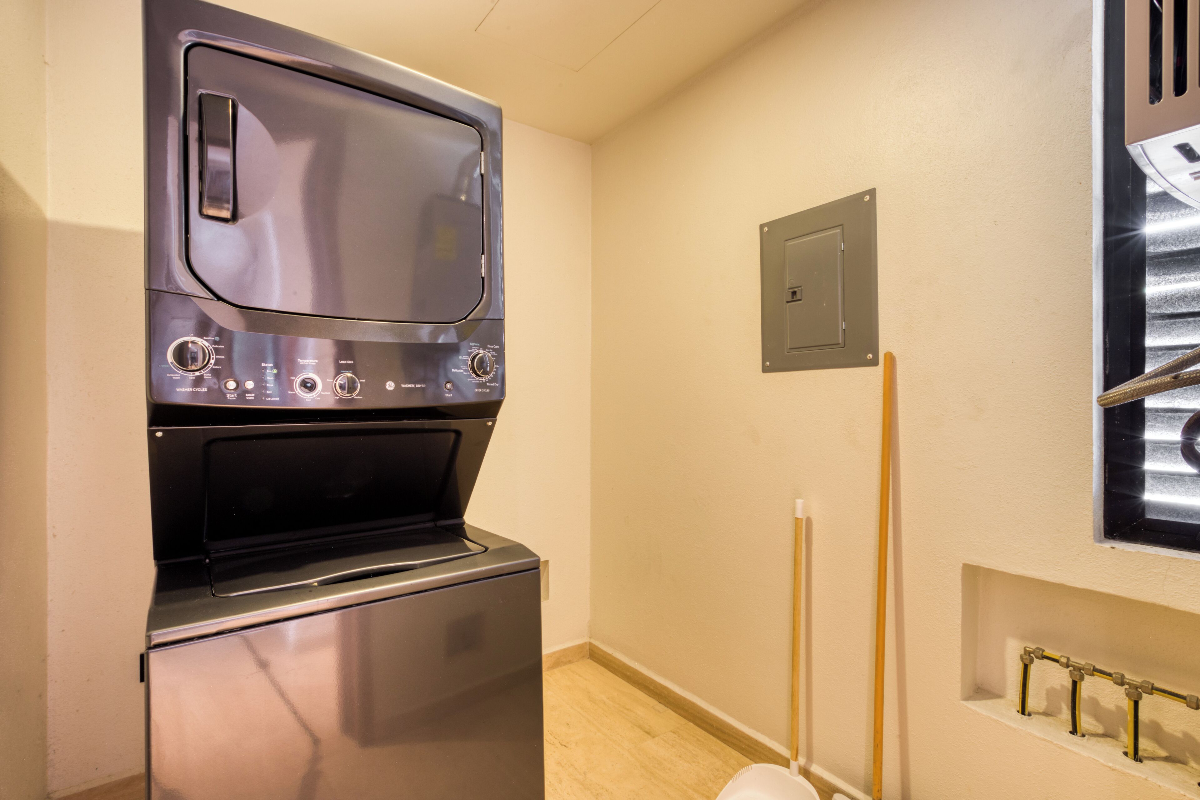 Een kleine wasruimte met een ingebouwde wasmachine en droger, een wandcontactdoos en een raam met jaloezieën.