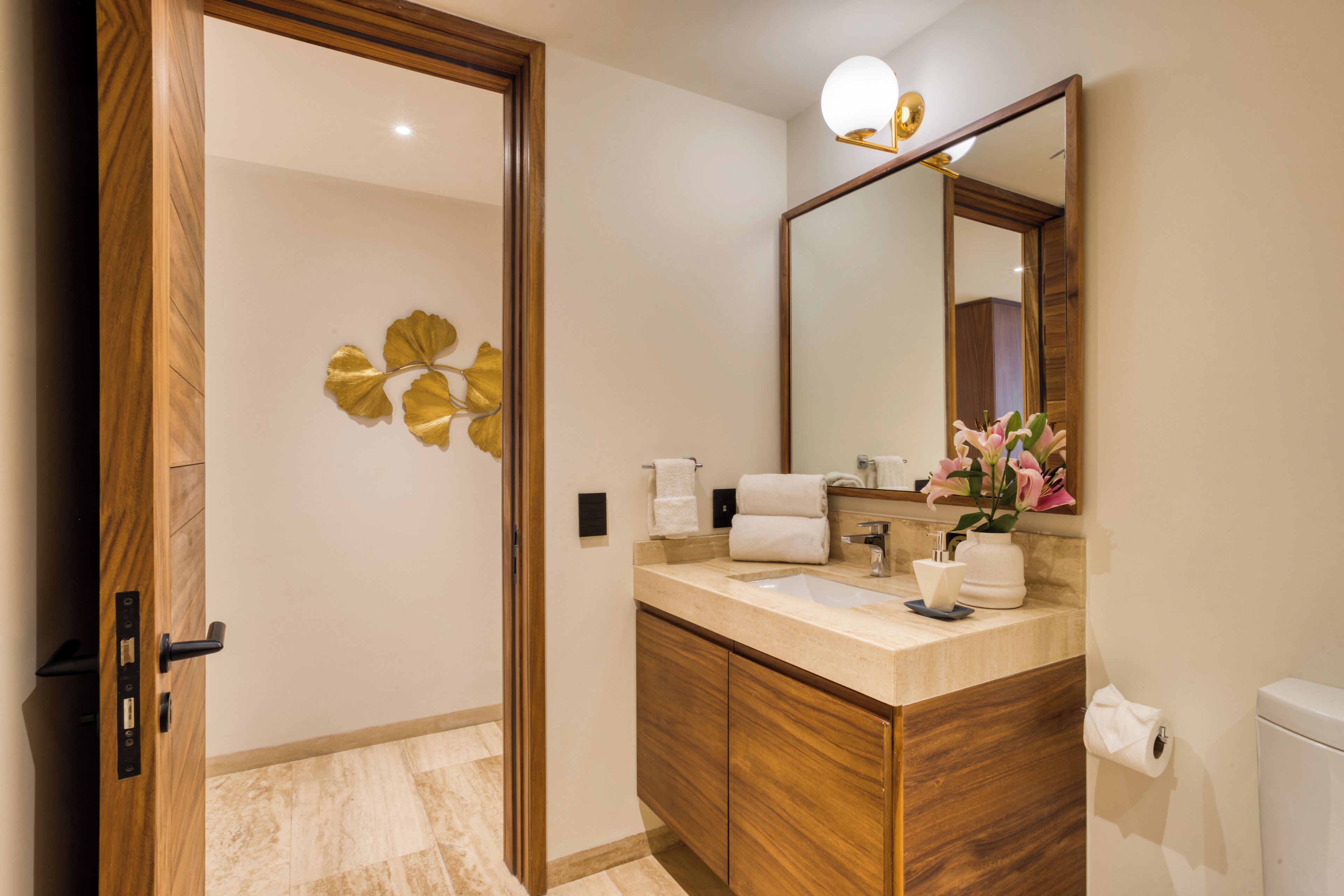 A modern bathroom with a wooden vanity, a large mirror, and a decorative wall piece.